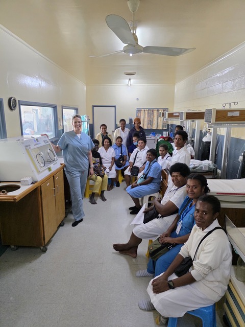 Medical specialist standing alongside healthcare workers and patients inside a hospital room.