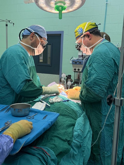 Two surgeons in surgical caps and masks performing a operation under operating room lights.