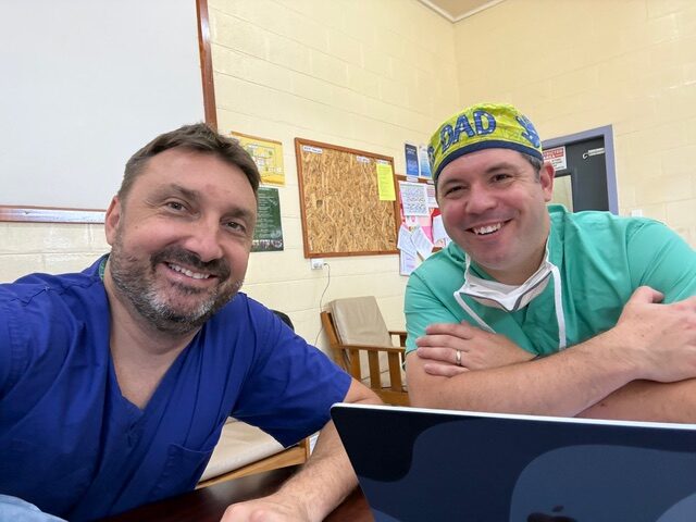 Two medical specialists smiling in surgical scrubs inside the clinic.